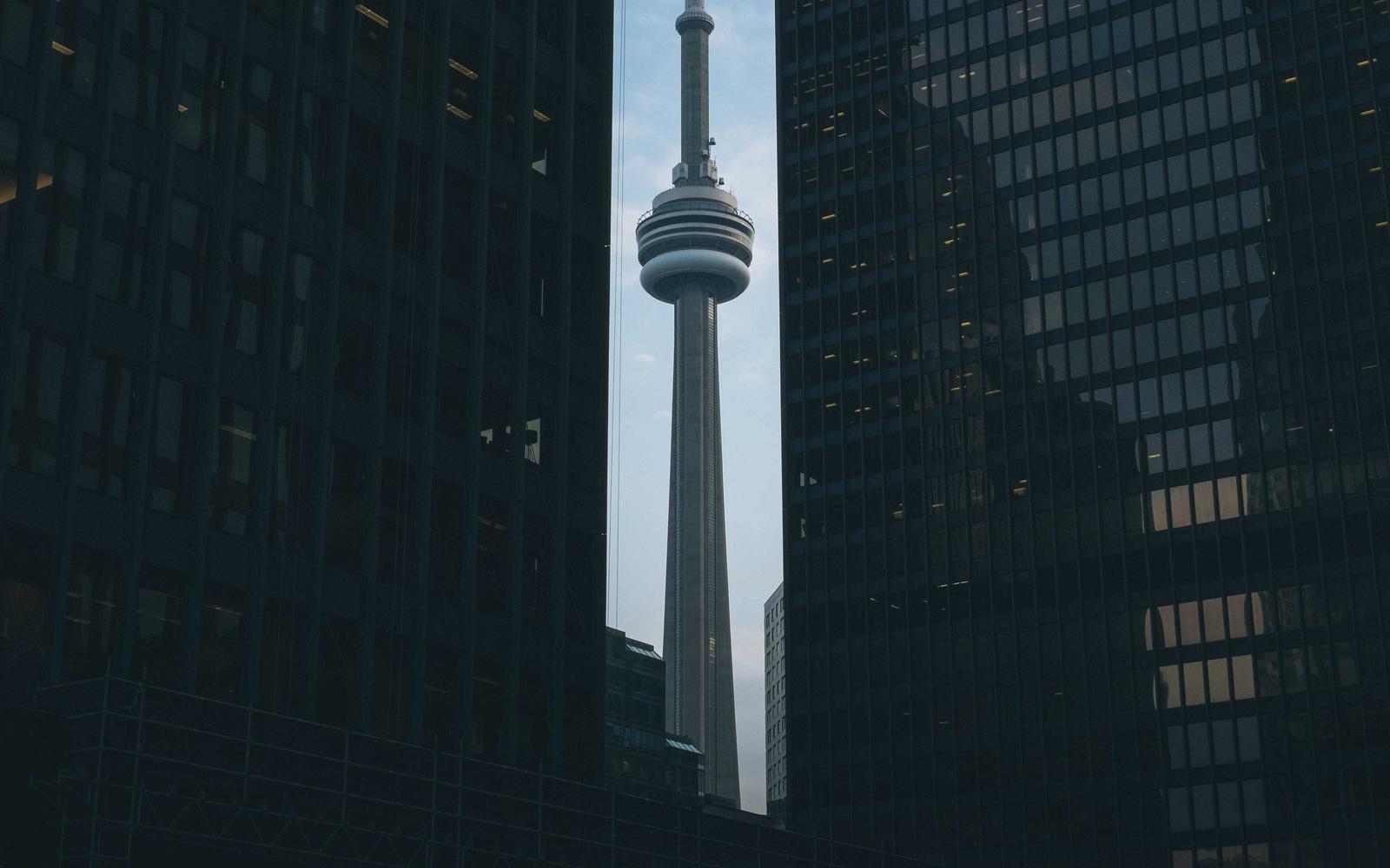 A slender communications tower framed between two dark glass office blocks
