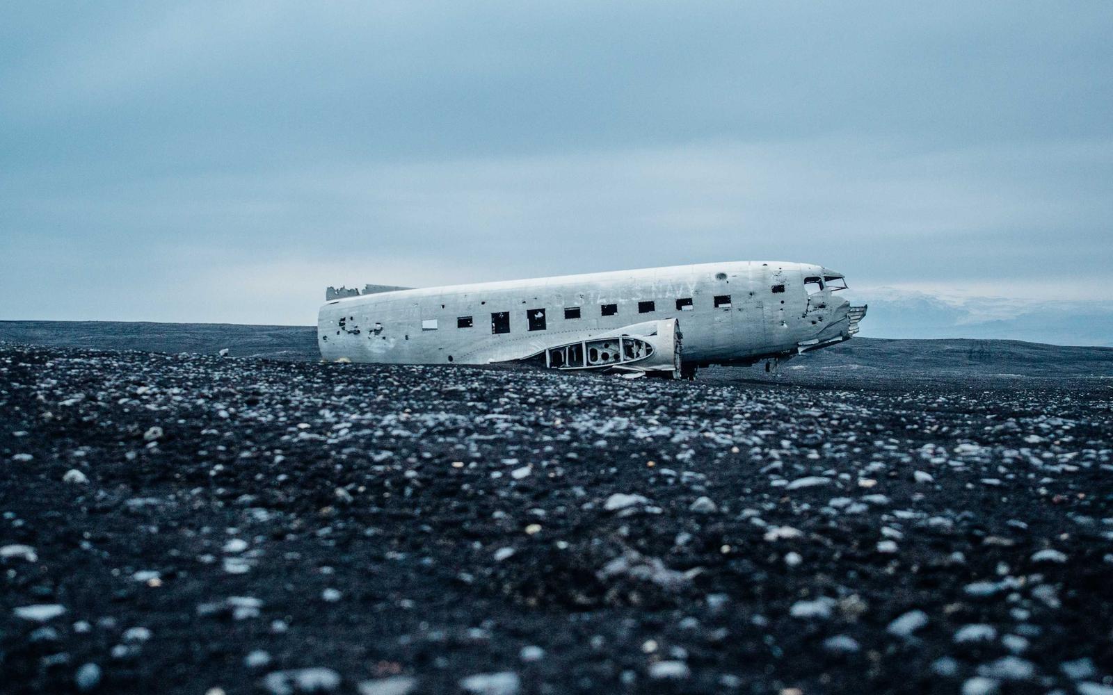 The stripped fuselage of a crashed aircraft resting on black volcanic gravel